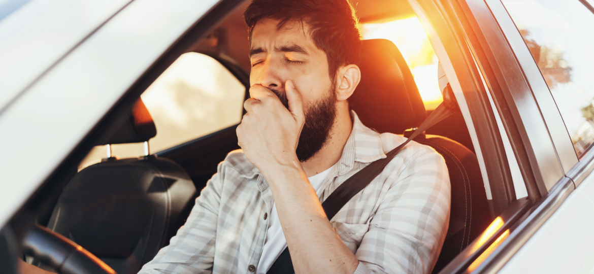 Tired man yawning while driving a white car